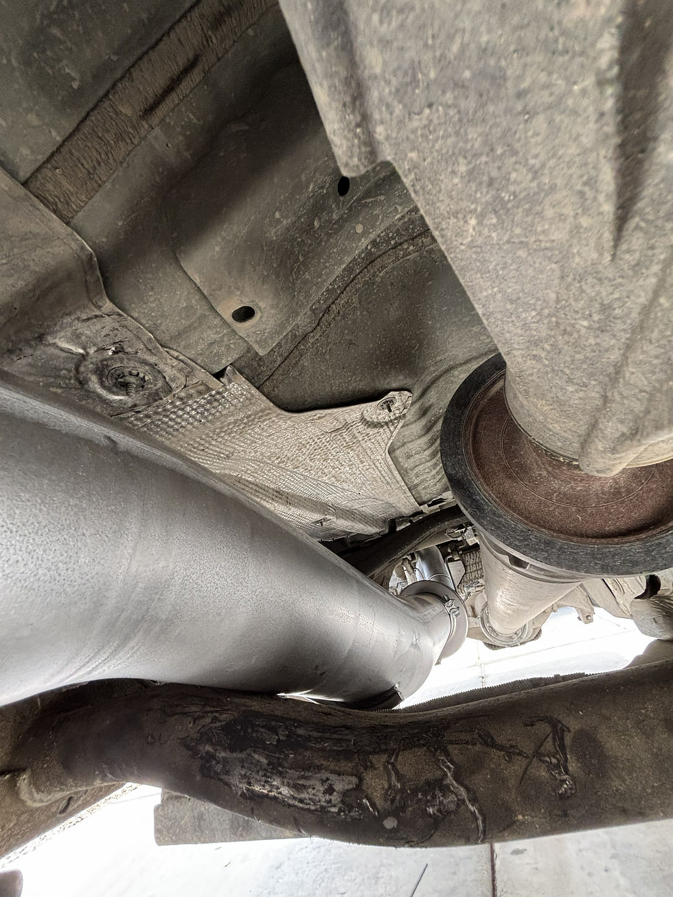 Close-up undercarriage view of a custom truck exhaust system and driveshaft, showing heat shielding and high-clearance piping.
