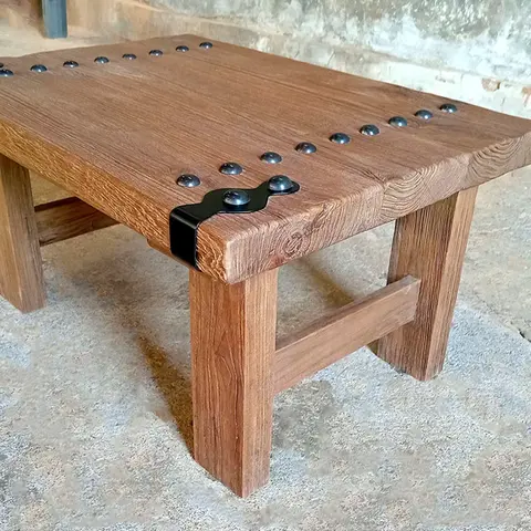 Close-up of rustic teak coffee table corner with hand-forged iron rivets and brushed wood texture, showcasing vintage Spanish-inspired design.