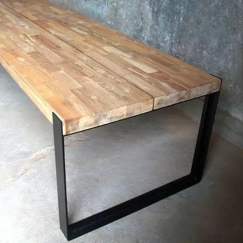 Close-up of smooth bleached teak wood grain and matte black iron leg connection on handcrafted dining furniture.