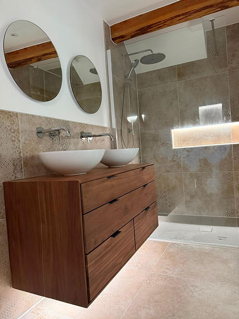 Luxury contemporary bathroom installation in South Hams featuring walk-in shower, floating wooden vanity unit, twin basins and designer Ca’Pietra tiles.