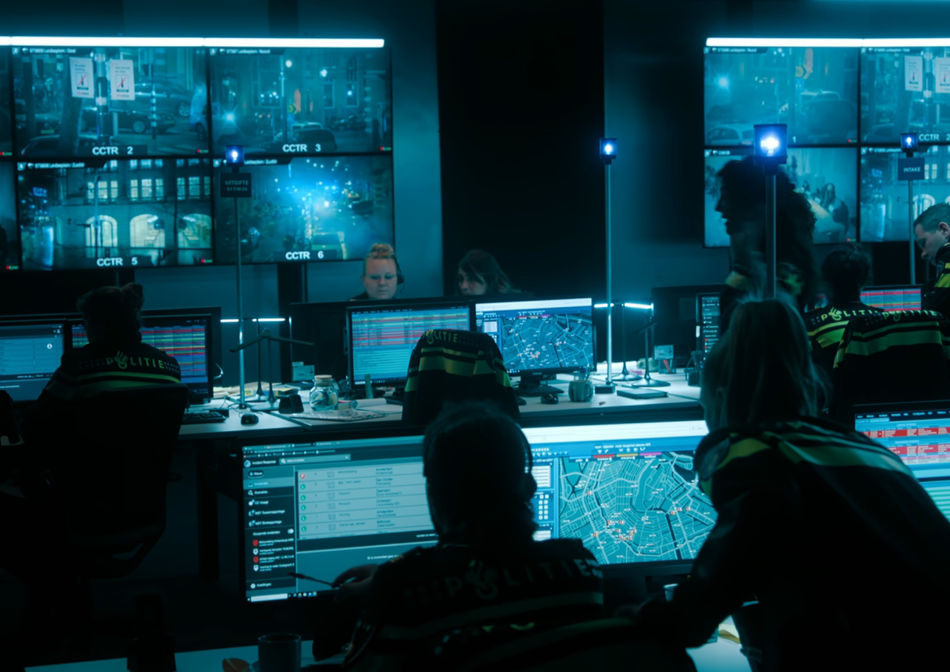 iHostage meldkamer filmset waar politie achter beeldschermen aan het werk is. videowall top de achtergrond met meerdere grote monitoren waar cctv systeem te zien is.