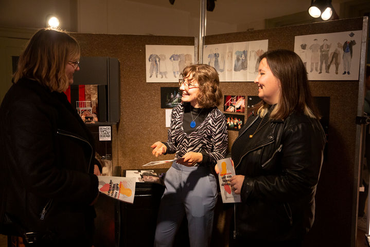Theatre designer, Victoria Maytom, discusses her designs with visitors at the exhibition. Costume designs are seen behind.