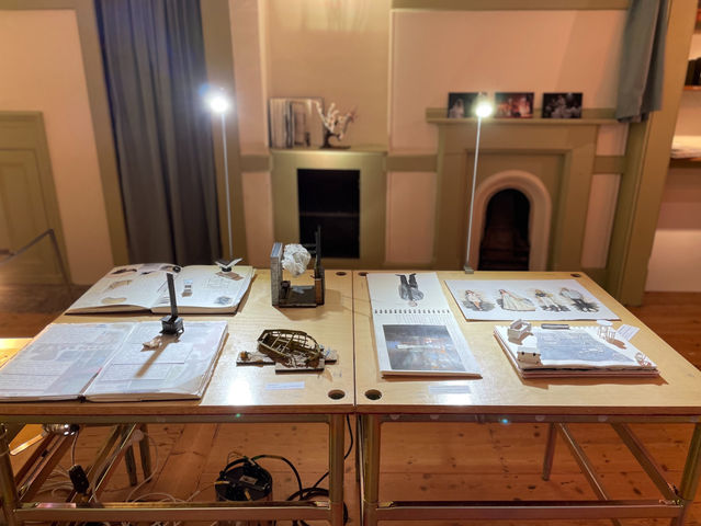 A photo of set and costume design sketchbooks and scale modelmaking laid out on a plinth at the Exhibition