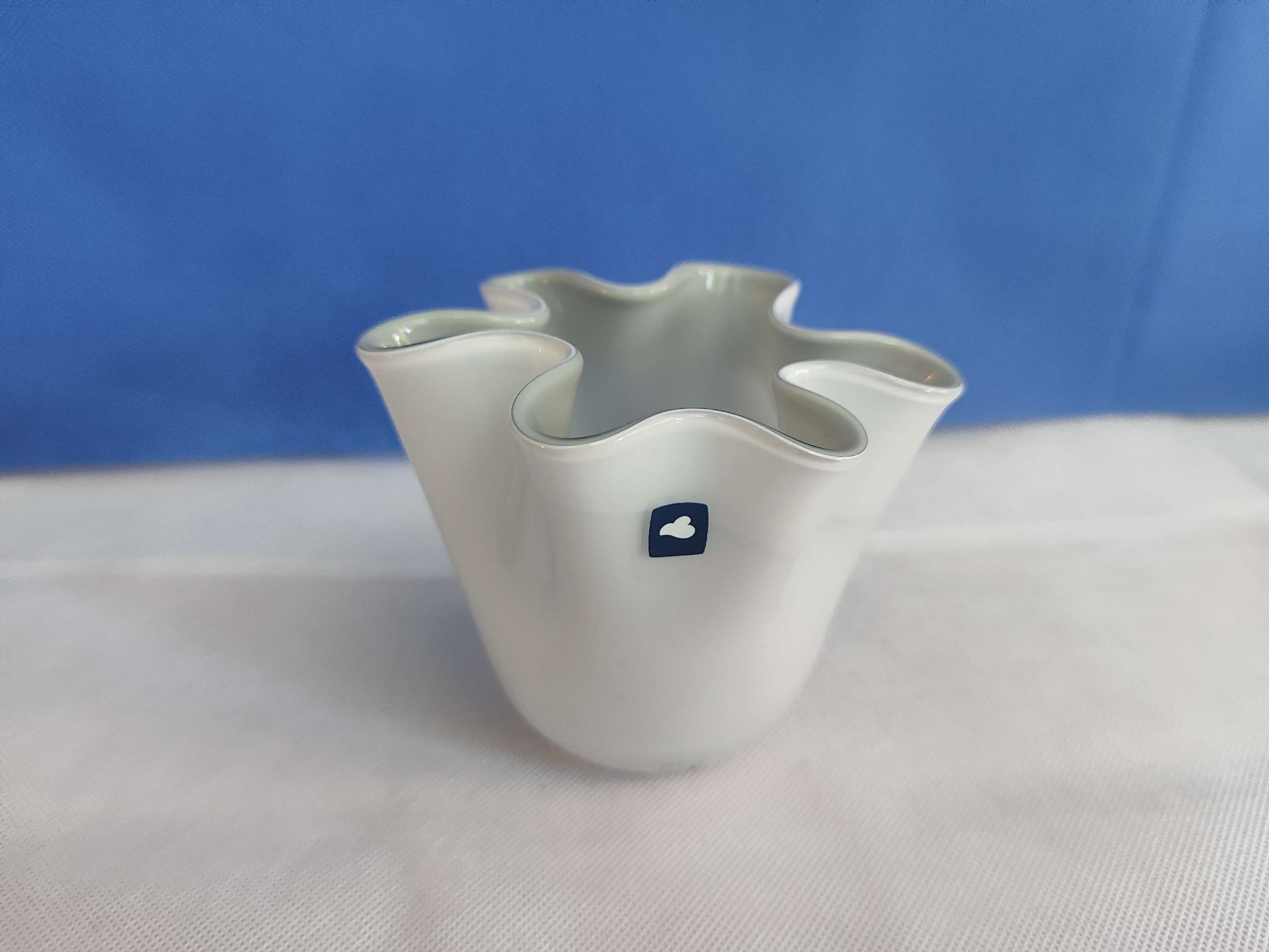 Photo of a vintage hand blown handkerchief vase with a cloud shaped sticker on it with a white surface and blue background