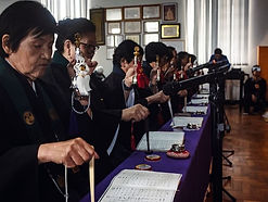 Registro do grupo Goeika cantando durante a Missa dos Antepassados, trajando vestimentas pretas e segurando instrumentos budistas utilizados na cerimônia.