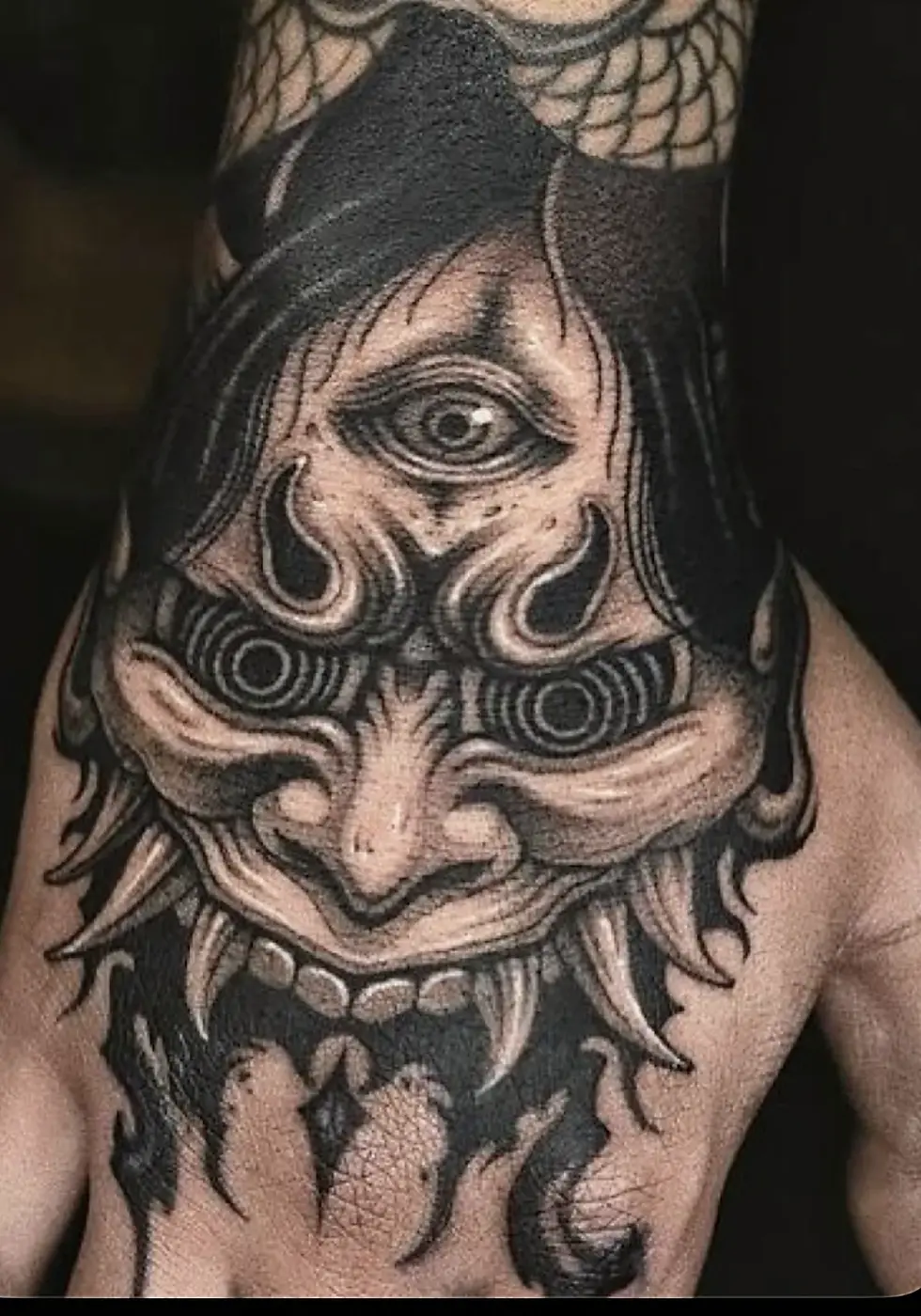 Black & Grey Tattoo mit Oni-Maske auf dem Handrücken