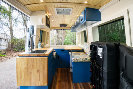 Ford Transit 148 custom van life conversion; foldaway seat, butcher block countertops with sink and folding counter extension, custom cabinetry and cushions