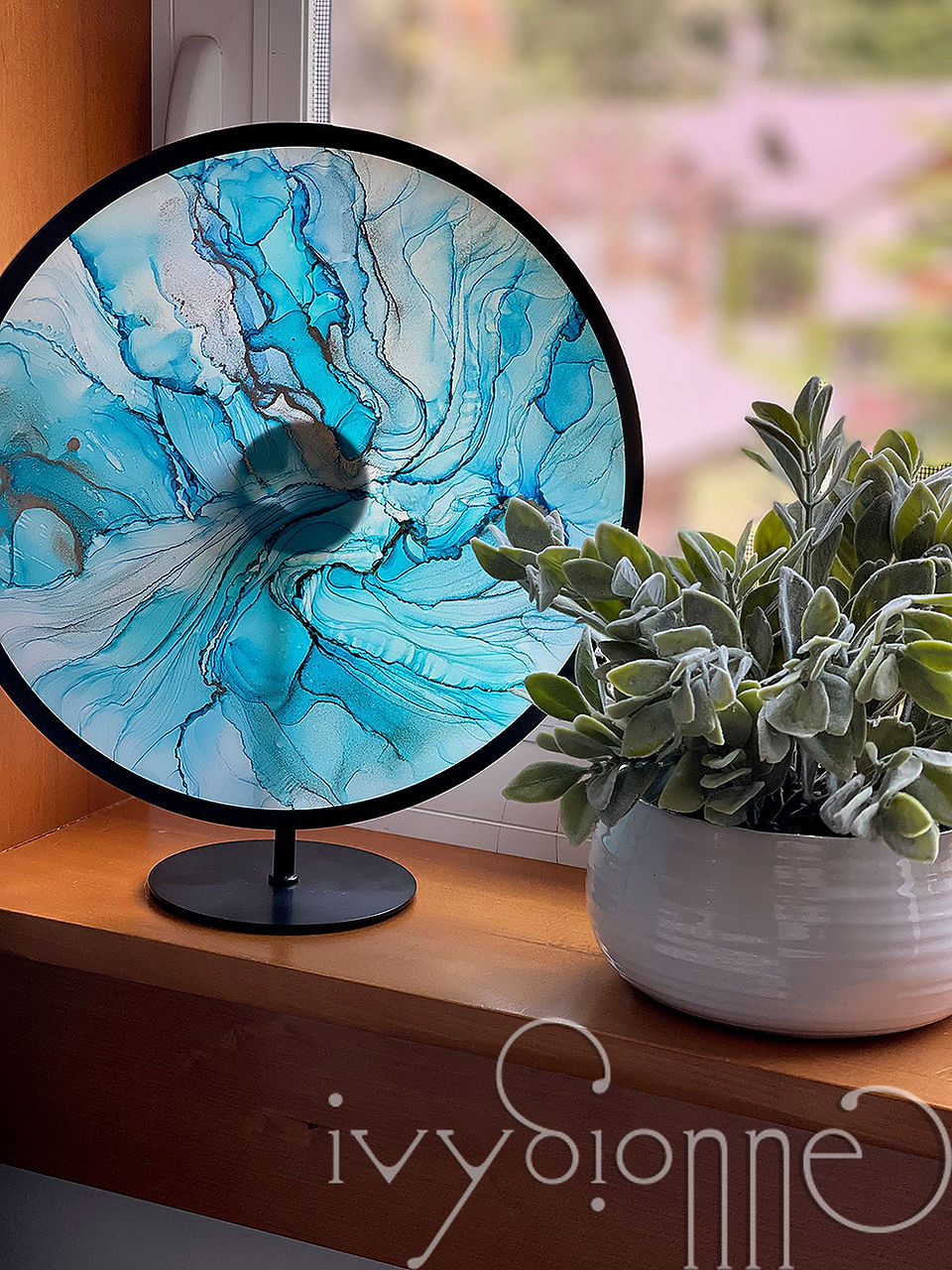 Alcohol ink glass painting in black infinity frame sitting on window ledge.