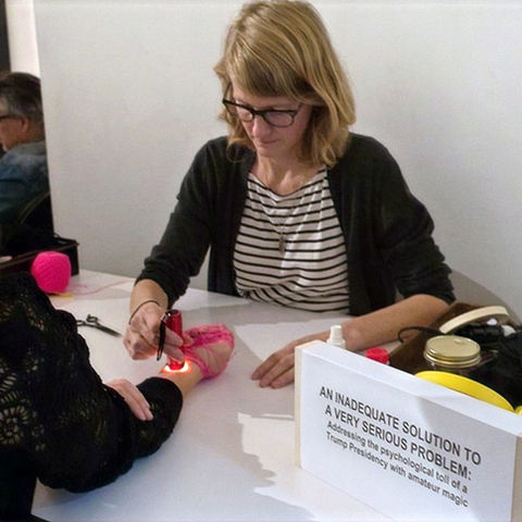 artist holding flashlight to a woman's wrist. hand wrapped in hot pink string.