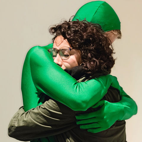 artist in green suit hugs woman with eyes closed.