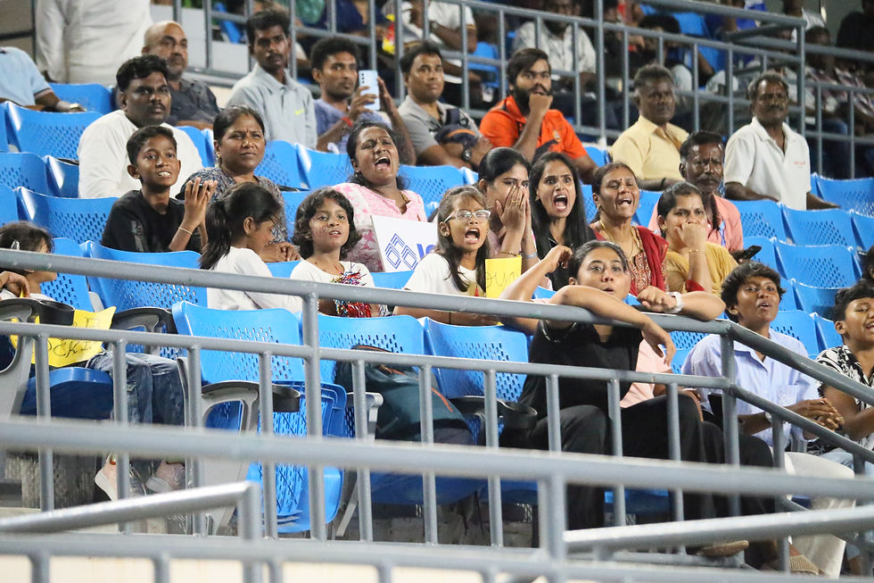 Crowd of excited spectators in blue stadium seats cheering and shouting, some holding signs, at a lively sports event.