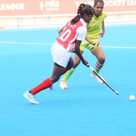 Women field hockey players in red-white #10 and neon green chase a ball on a blue pitch, with Hockey League banner.