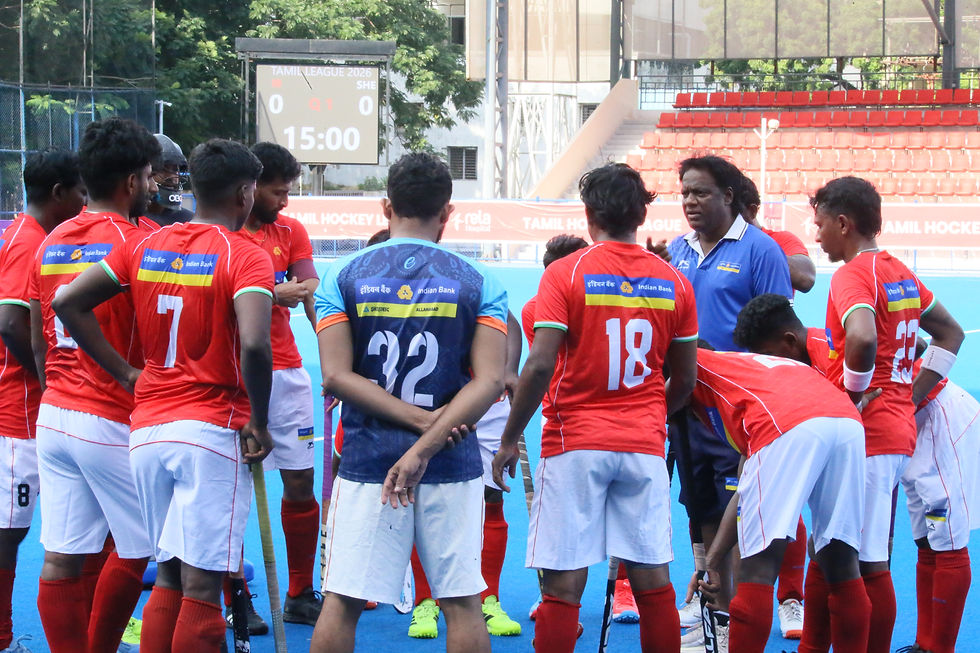 Hockey team huddles with coach on blue field; scoreboard shows Tamil League 2026, 0-0, 15:00, in an outdoor stadium. Olympian Thirumal Valavan at Tamil Hockey League