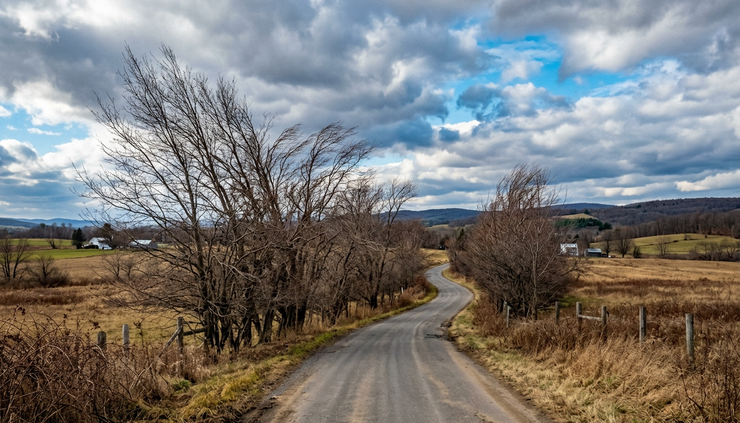 Wide-angle view of a windswept rural road under broken clouds in Central New York.