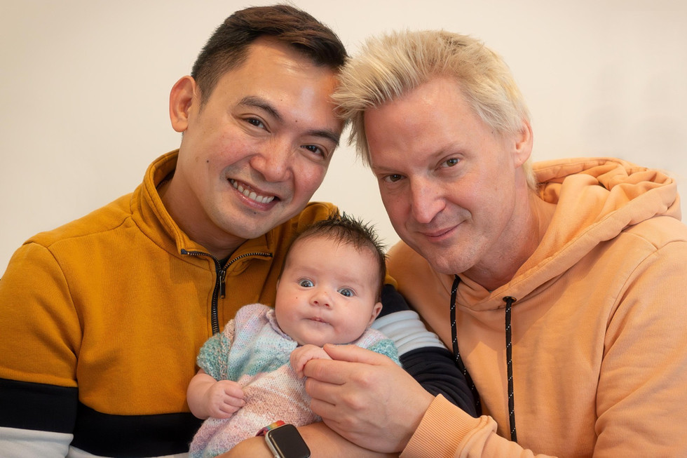 Chris Sta. Brigida-Kopp and his partner smile while holding their daughter during an intimate family portrait.