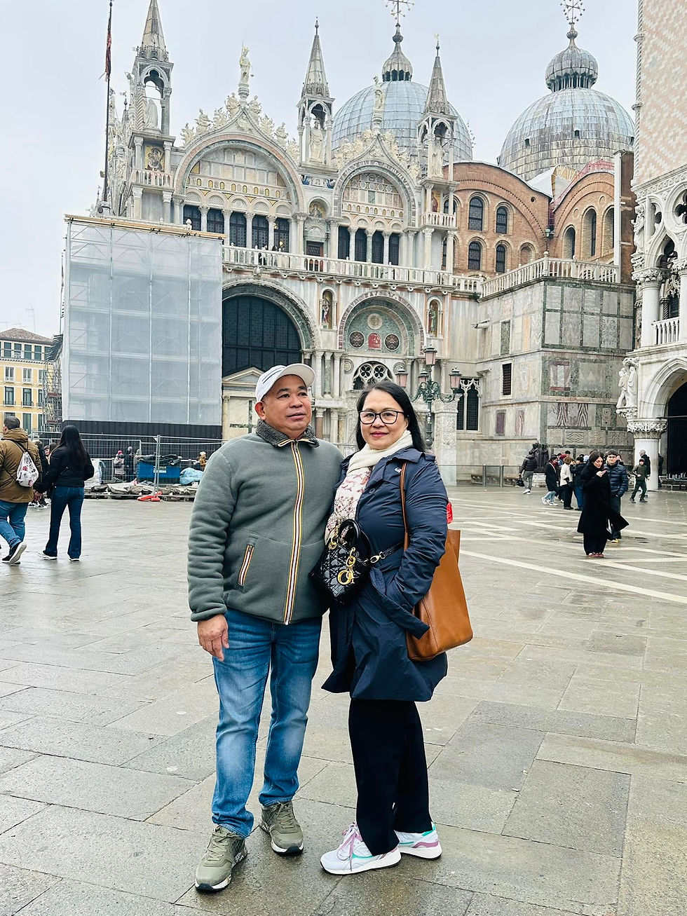Mercy Malabanan and her husband standing together in St Mark’s Square, Venice, with the basilica’s ornate façade and domes behind them.