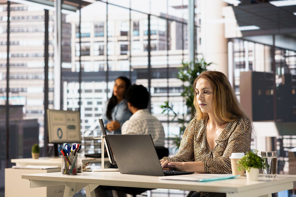 Woman working in an open space office with large windows and co-workers in background