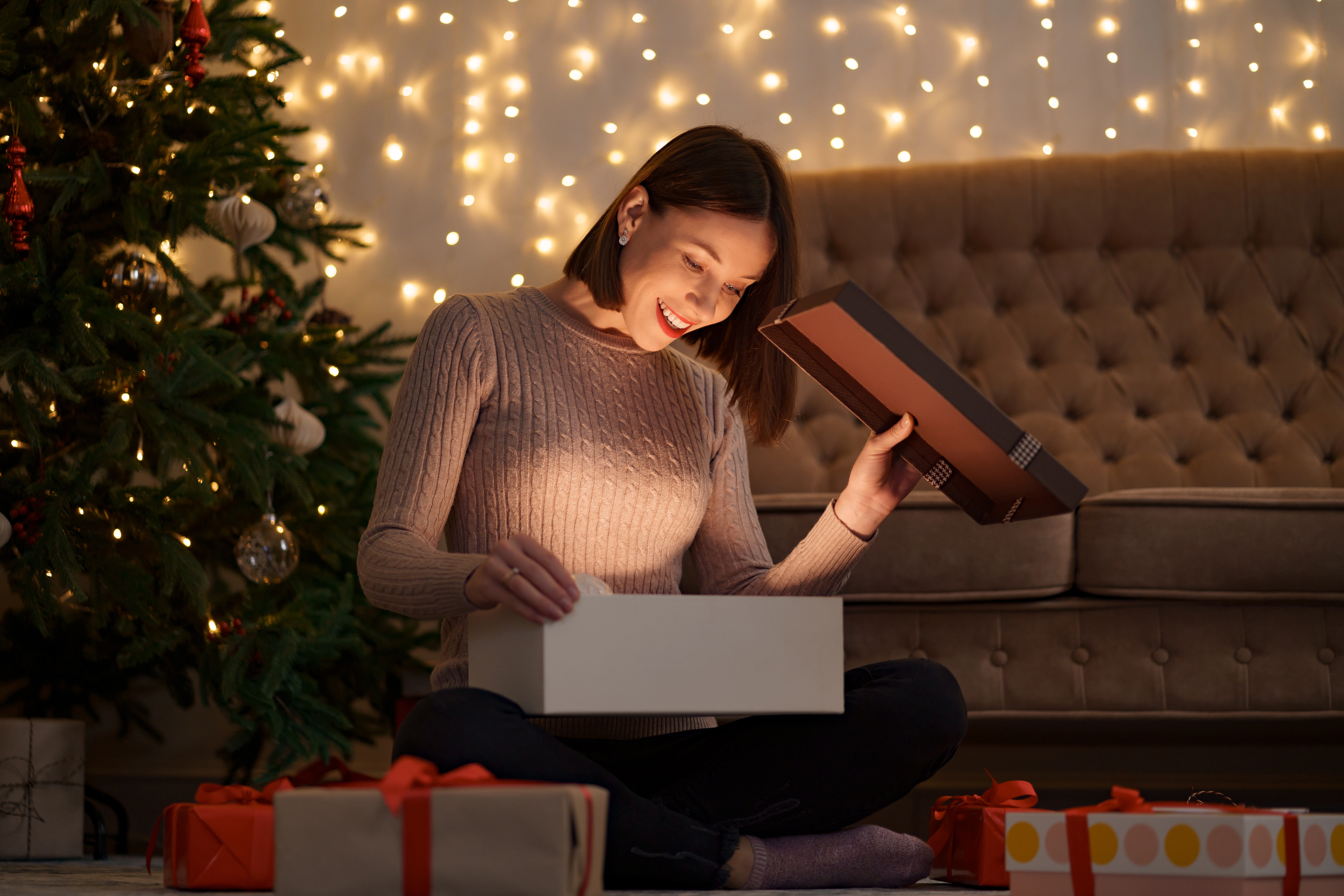 This image shows a customer opening a festive poly mailer. The customer is smiling and excited, and they are holding up the mailer to show the contents. The mailer is filled with gifts, and there is a festive ribbon tied around it.