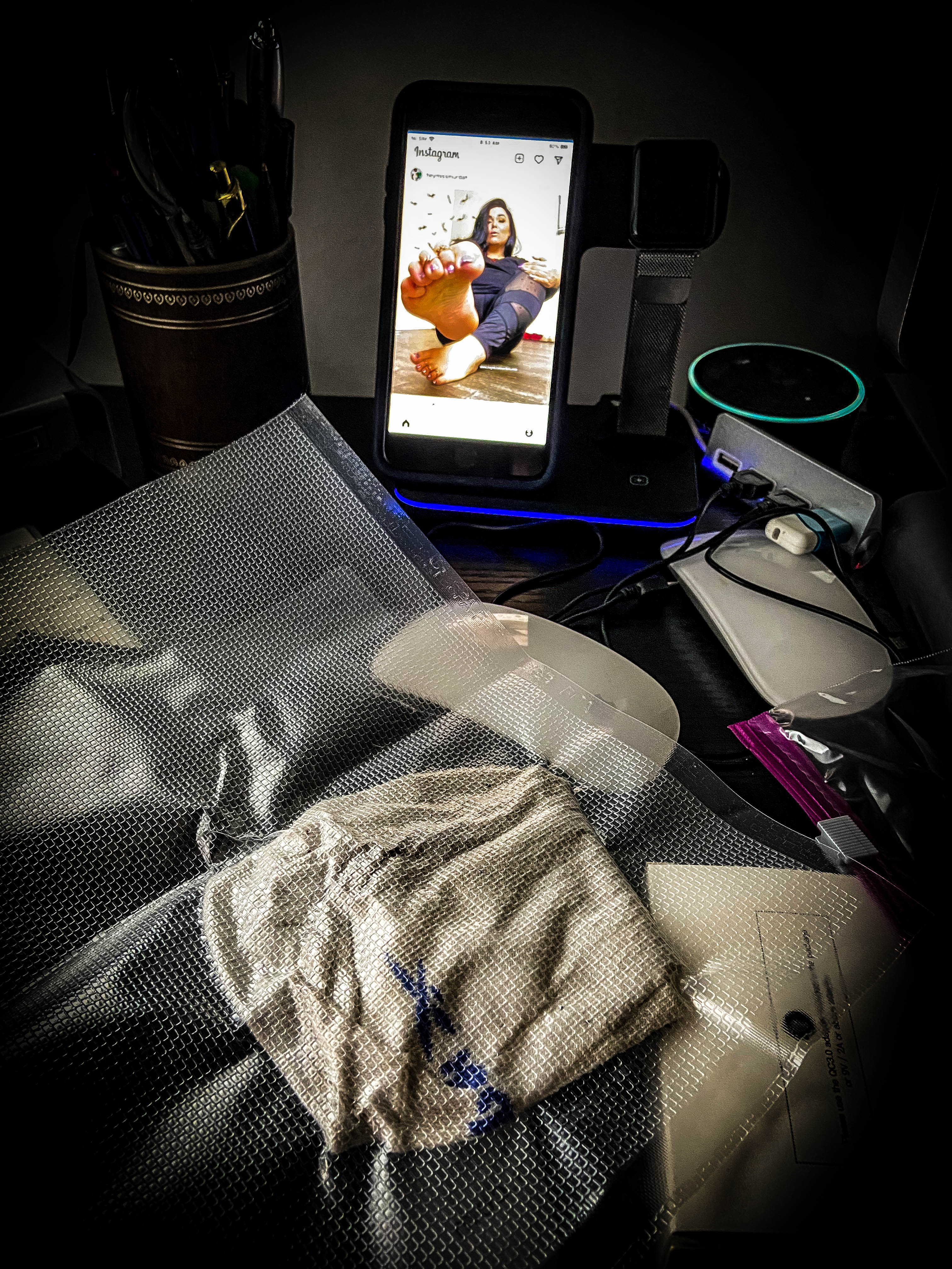 Nurfusee.com presents for foot fetish enthusiasts Miss Murdah vacuum-sealed socks on my desk, and an image of Miss Murdah is displayed on my cellphone.