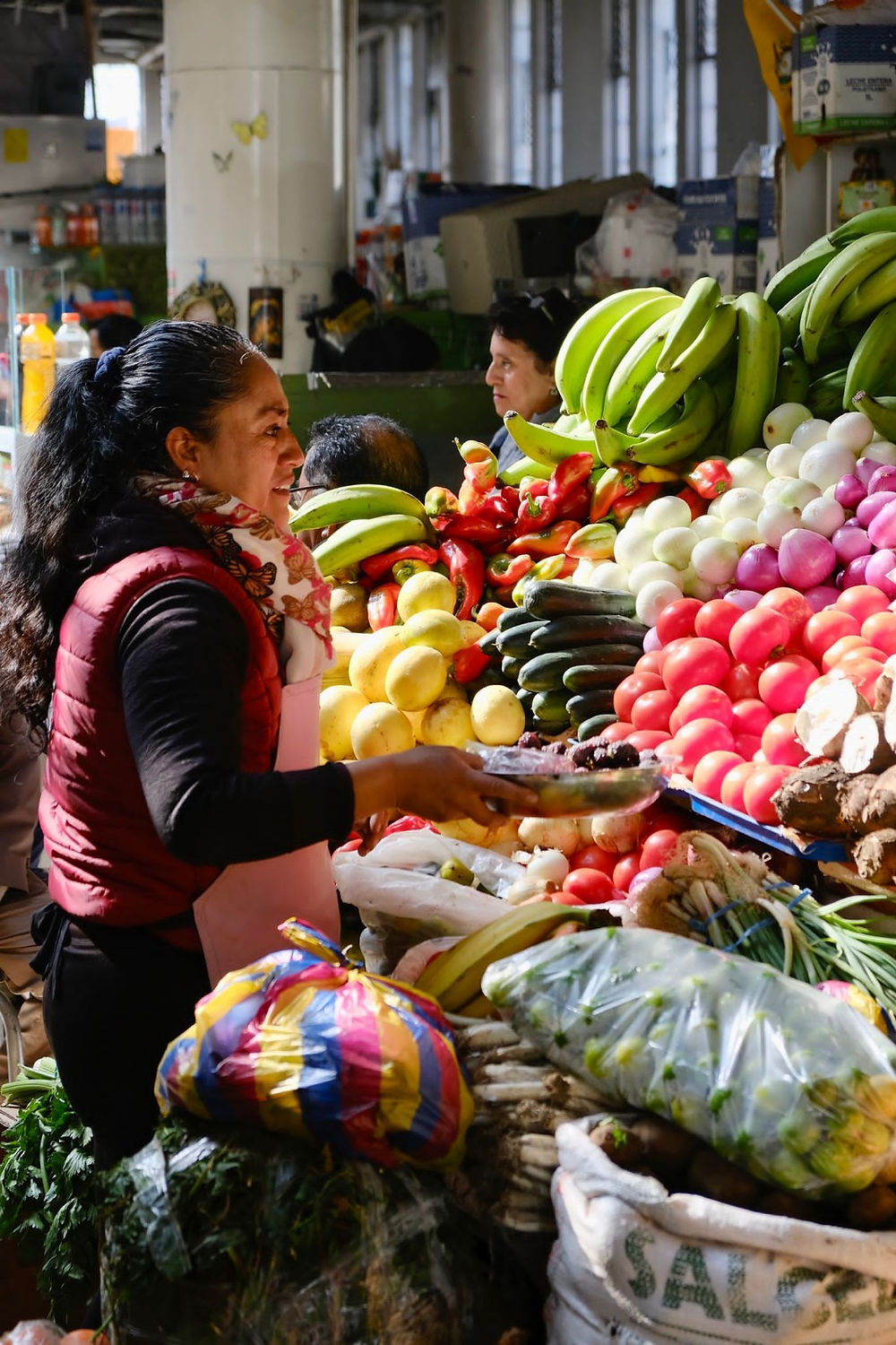 Woman arranging colorful produce at a market stall.
