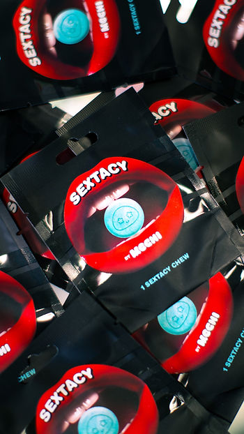 Packets labeled "Sextacy by Mochi" with red lips design, containing blue chews. Pattern formed by arranged packets on a black background.