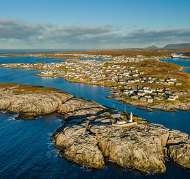 A drone image of a coastal community during the fall. Houses are nestled along the coastline and on a nearby island is a lighthouse.
