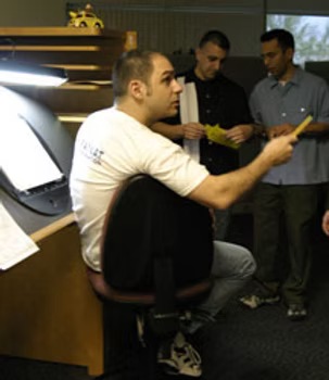 Len at an animation desk, turning in his chair to talk through a drawing with two colleagues