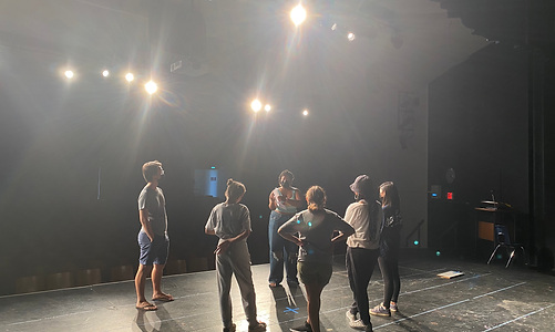 A small group of high school students stand in a circle onstage together during an after school program