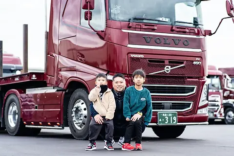 株式会社山幸運輸のトラックの前で2人の子供を抱えた男性従業員