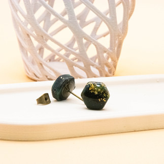 Dragon Eye Little Stud Earrings | Hexagon Shaped | Black, Green and Gold Marble Effect | presented lying on a beige trinket tray with one earring facing towards and the other facing away to show the stud details and butterfly back.