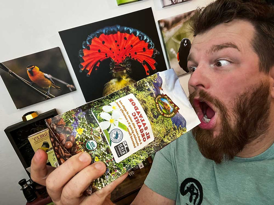 a man with a beard pretends to eat coffee beans from a vibrantly colored coffee bean bag