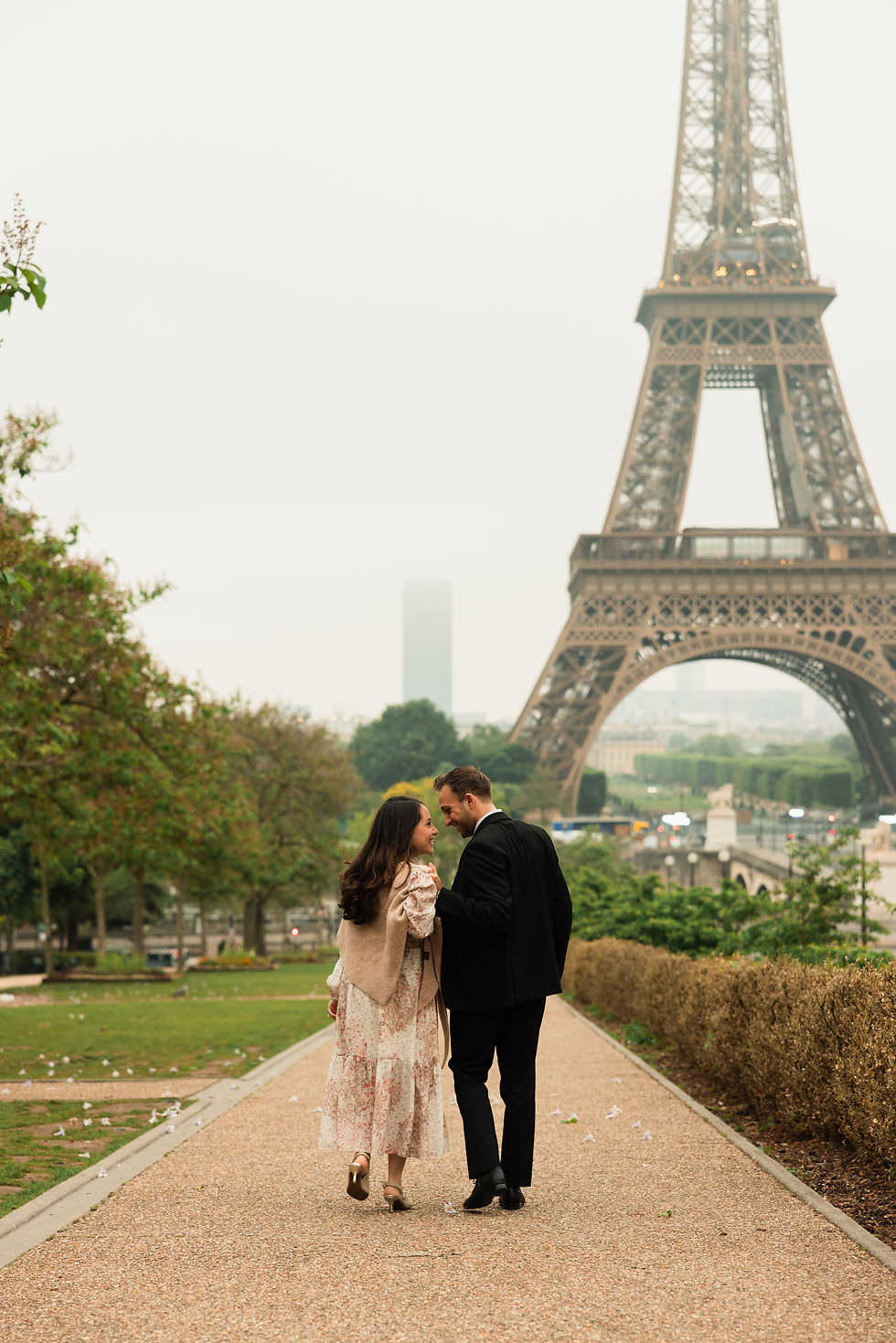 Couple walking hand in hand toward the Eiffel Tower on a tree-lined path in Paris, with a soft, romantic mood.