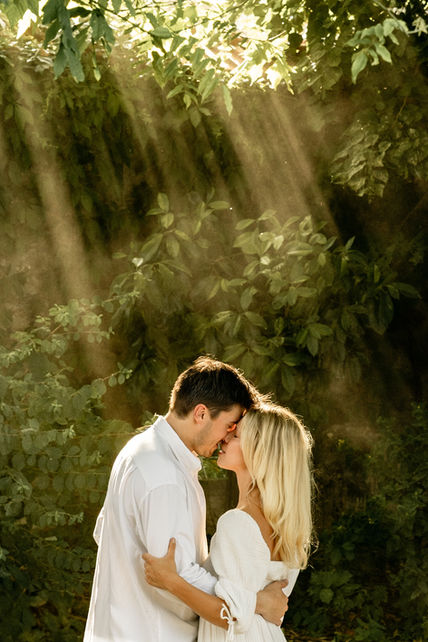 Woman and man embracing in a forest under golden rays of light.