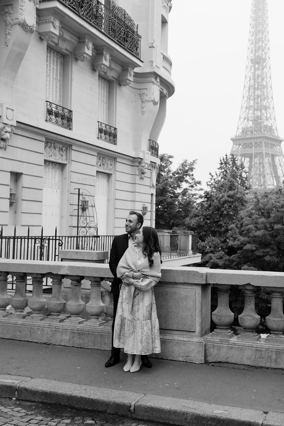 Black-and-white couple posing on a Paris balcony with the Eiffel Tower in the background.