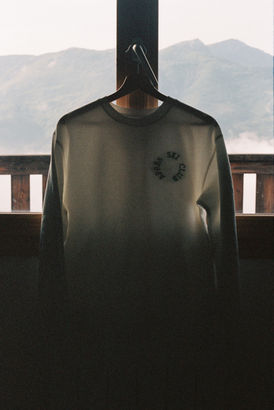 The classic Après Ski Sweater hanging on a window with mountains in the background
