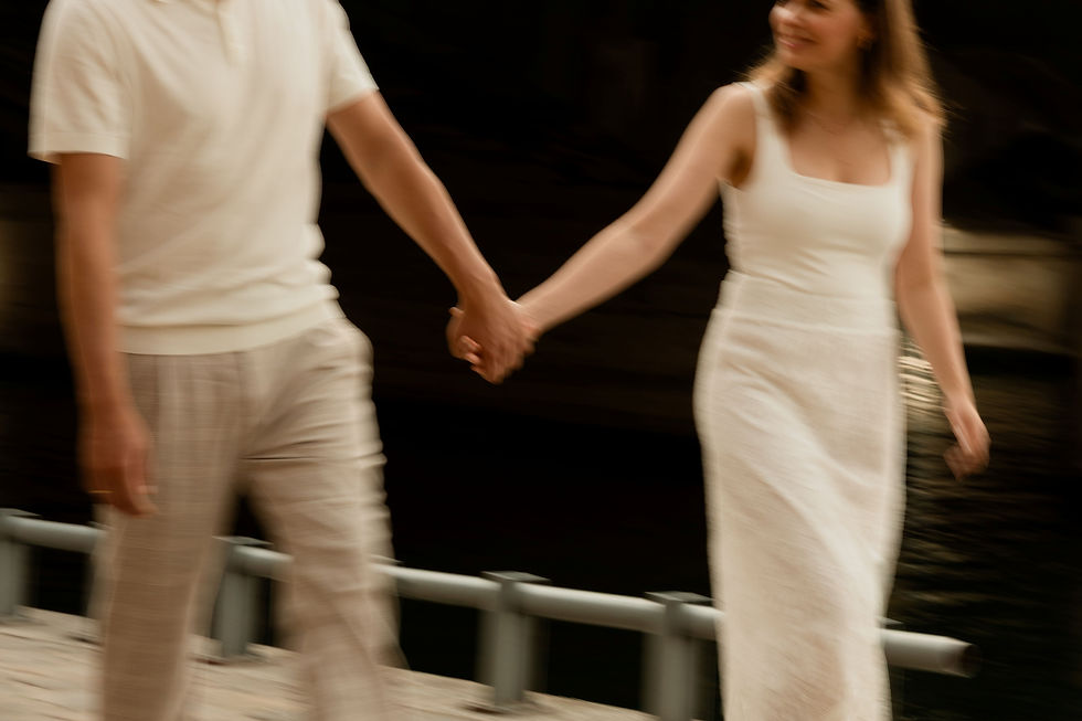 Blurred image of a couple holding hands, walking on a path by the Seine. Both wear white outfits, with dark background and joyful expressions.