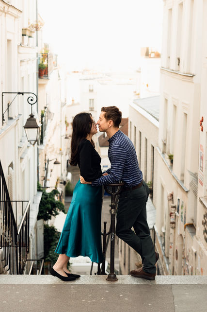 A couple touch noses at the top of a staircase in Montmartre, overlooking Paris.