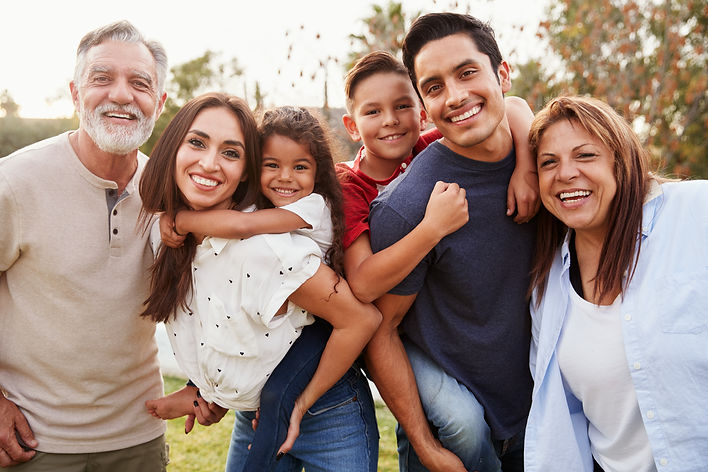 Three generation Hispanic family standing in the park, smiling to camera, selective focus.