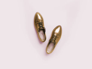 Gold shoes on a pale pink background, neatly placed side by side. The image has a clean, minimalist aesthetic.