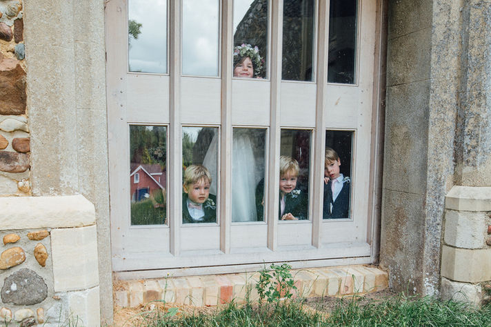 A flower girl and page boys peer out of a window at a wedding, captured by Tara Gillen Photography