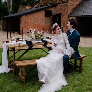 Bride and groom sitting at a rustic table with boho festival inspired table decor at an outdoor wedding photoshoot at Turvey House in Bedfordshire