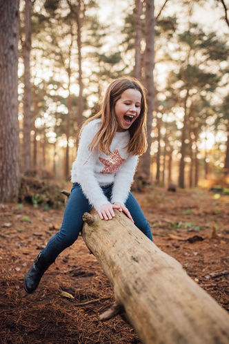 A girl having fun playing on a log see-saw during a family photoshoot with Tara Gillen Family Photographer in Bedford