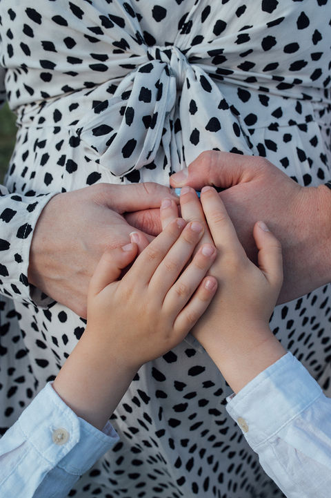 A family of four hold hands on the mother pregnancy bump during a maternity photoshoot with Tara Gillen Photography in Bedford
