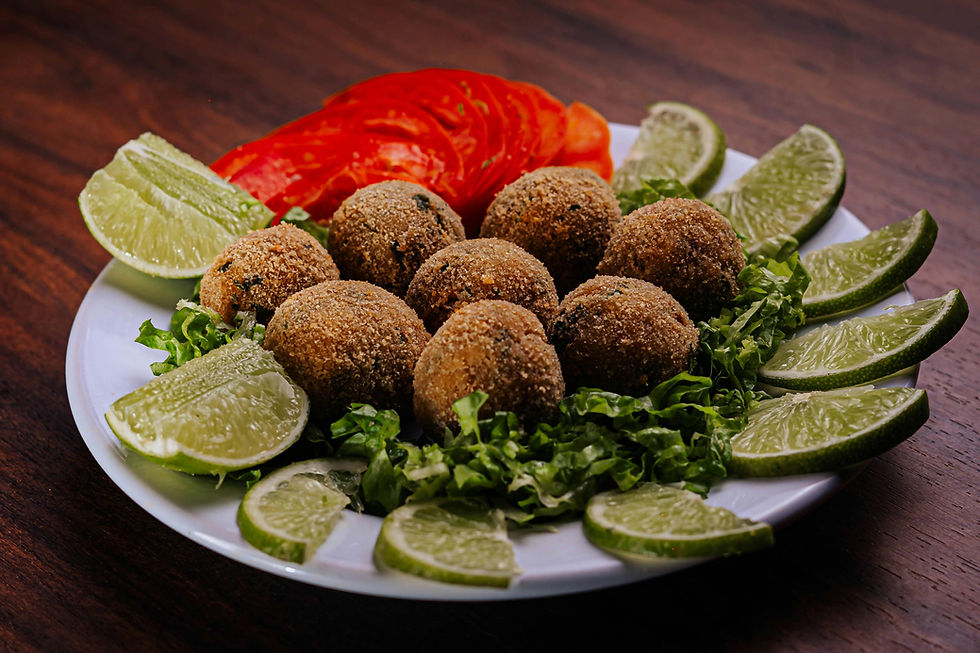 Plate of fried croquettes on lettuce, surrounded by lime and tomato slices. Dark wooden table setting.