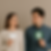 Man and woman holding heart and dollar signs stare at each other seriously. Neutral beige background.