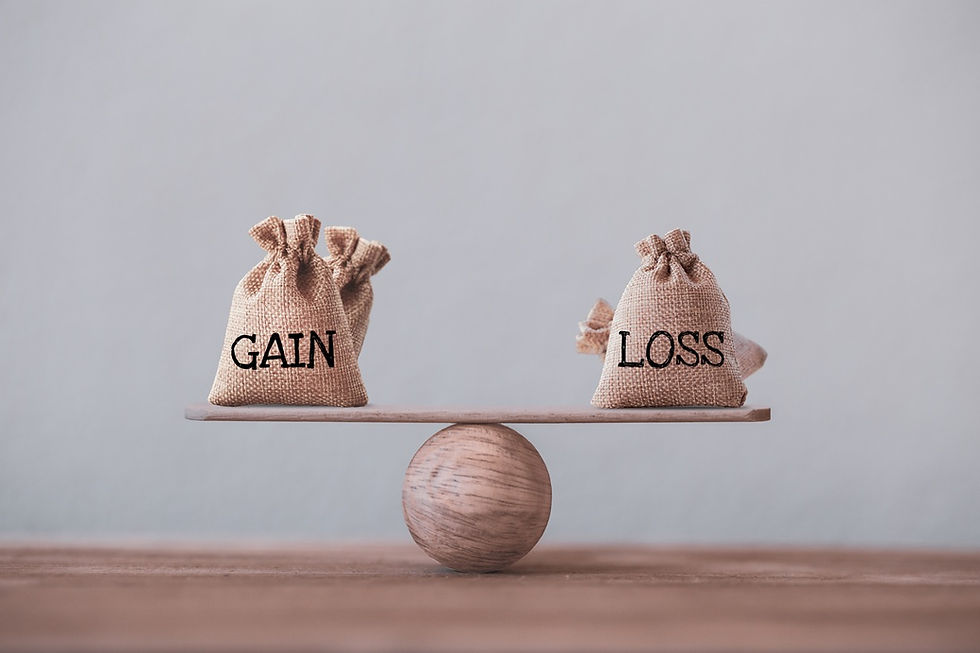 Two burlap bags labeled "GAIN" and "LOSS" balance on a wooden plank atop a sphere, symbolizing equilibrium. Neutral background.
