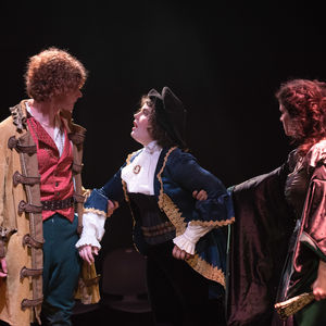 Viola of Twelfth Night is confronted by Olivia and Orsino. Soft white light illuminates Viola's face, The others' face are shadowed, and they are backlit by light reds.