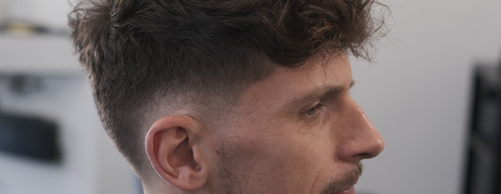 Textured crop cut with a drop skin fade, Longer curls with texture on top and the hair is styled forward. Styled with Sea salt, Profile View