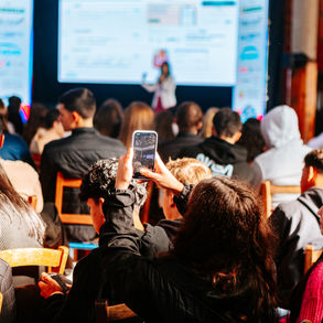 Pessoa grava apresentação em tela grande com smartphone em evento.