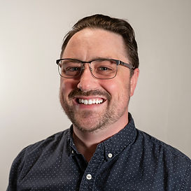A professional photo of a man wearing glasses and a blue button up shirt smiling at the camera